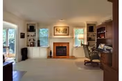 Living room with a central fireplace flanked by built-in shelves and cabinets, windows, a desk and seating.