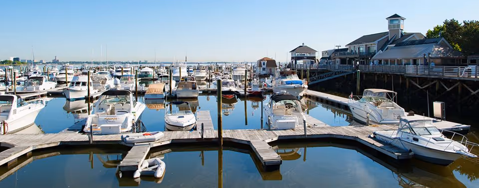 Marina with boats docked at wooden piers and a waterfront building under a clear blue sky.