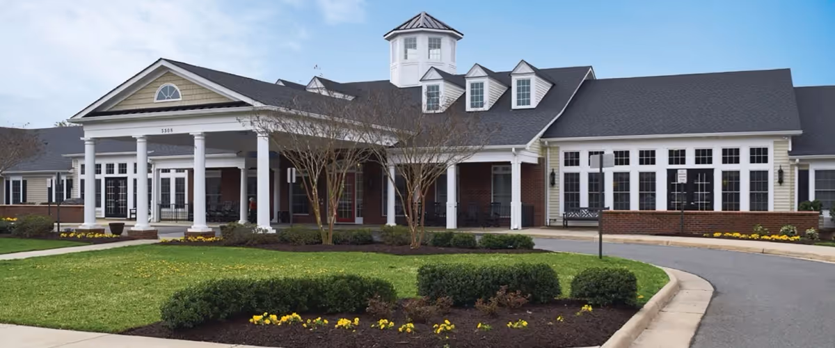 A single-story senior living facility with brick and beige facade, white columns, and curved driveway.