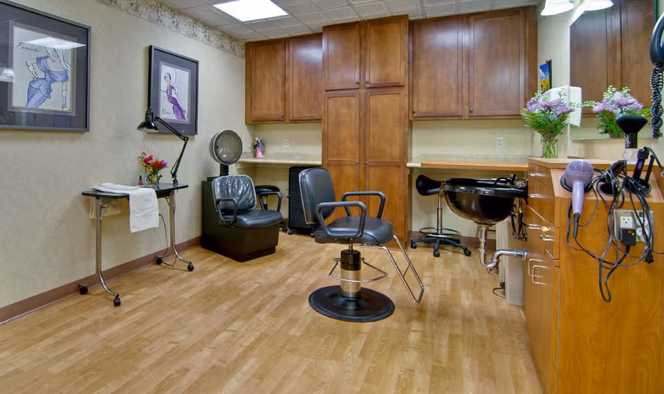 Interior salon room with styling chairs, a shampoo sink, wooden cabinets, and hairdryers on the counter.