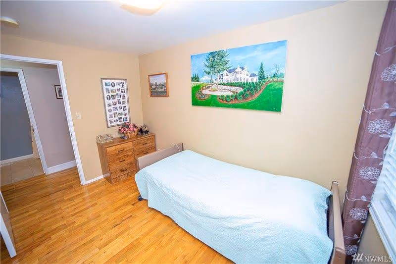 Small bedroom with a single bed, wooden dresser, hardwood floor, and a landscape painting on the wall.