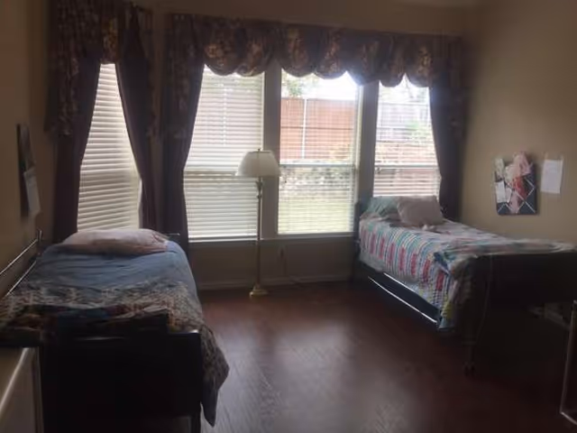 Two twin beds flank a central lamp by large, curtained windows.