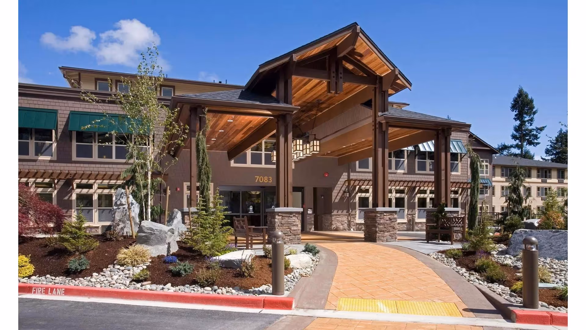 Front entrance of The Lodge at Mallard's Landing showing a covered wooden porte-cochere, paved walkway, and landscaped grounds.