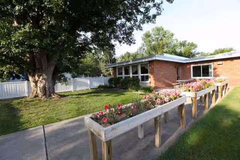 Exterior view of Laurels of Mt. Pleasant with brick building, walkway, and blooming planters.
