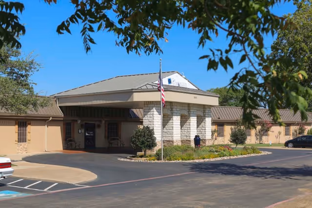 Exterior view of Carrollton Health & Rehabilitation Center building with a flagpole and landscaped area in front, framed by tree branches under a clear blue sky.