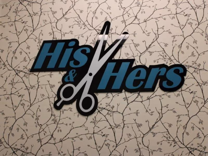 A decorative sign on a wall with a pattern of thin branches and leaves. The sign features the words 'His & Hers' in blue and black letters, with a large pair of scissors integrated between the words.