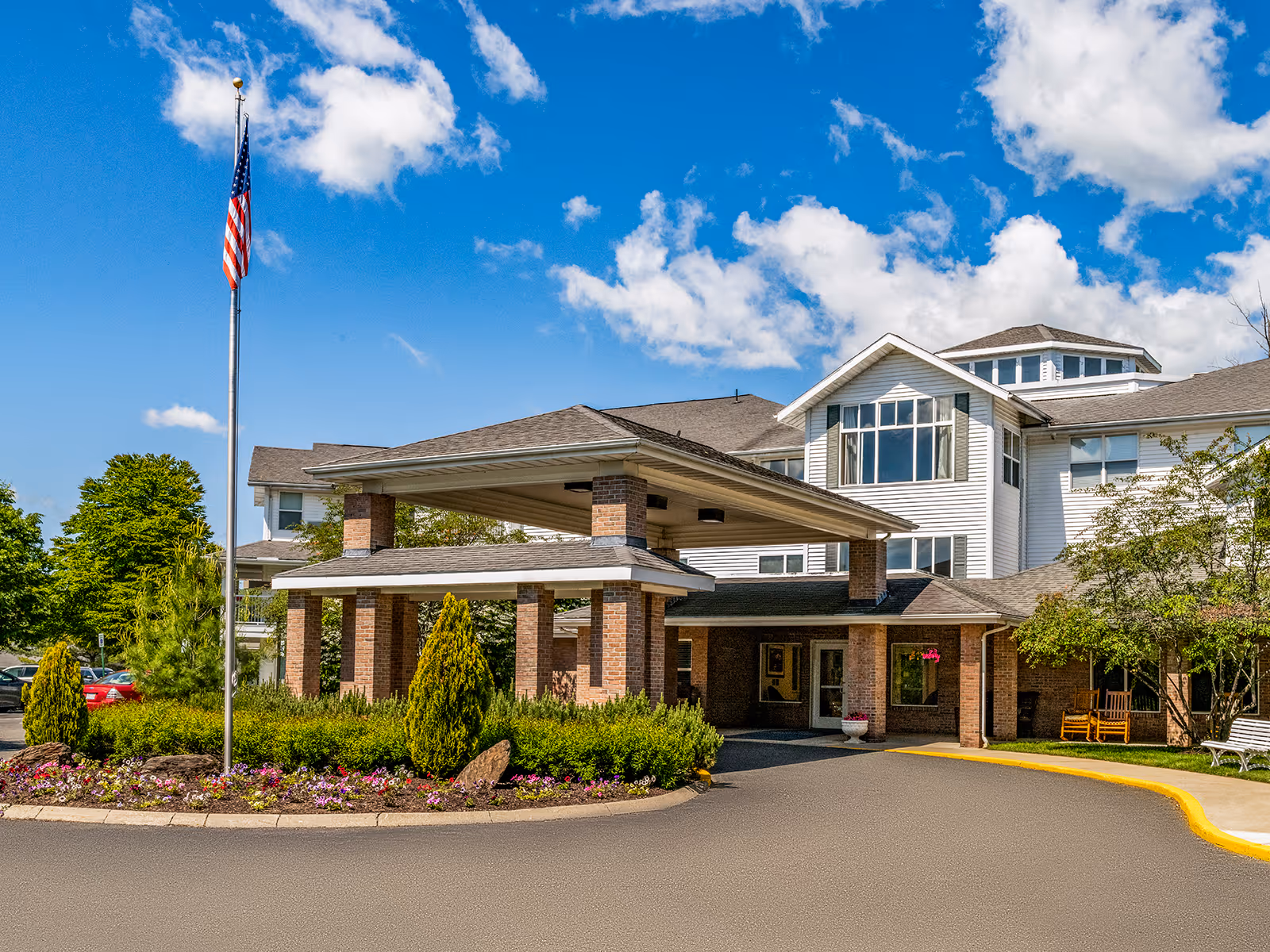 A senior living facility entrance with brick columns, a porte-cochère, and landscaped grounds.