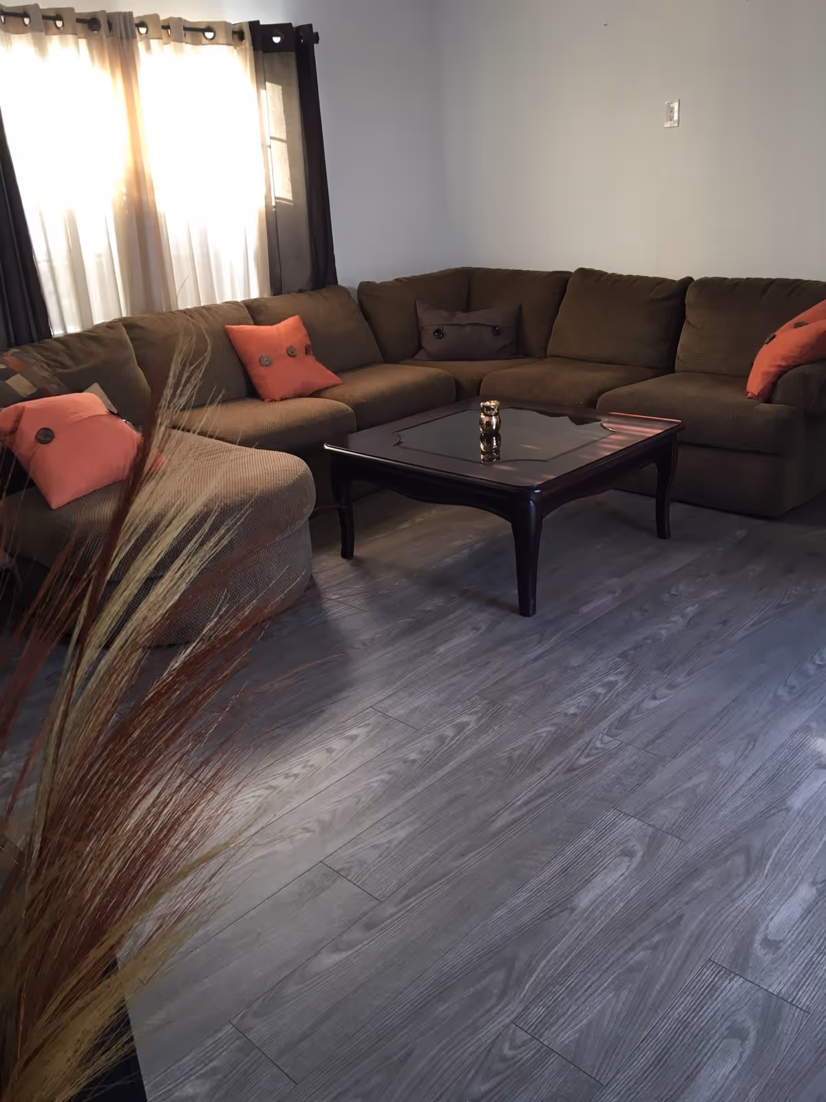 A cozy living room with a brown sectional sofa, orange pillows, and a coffee table.