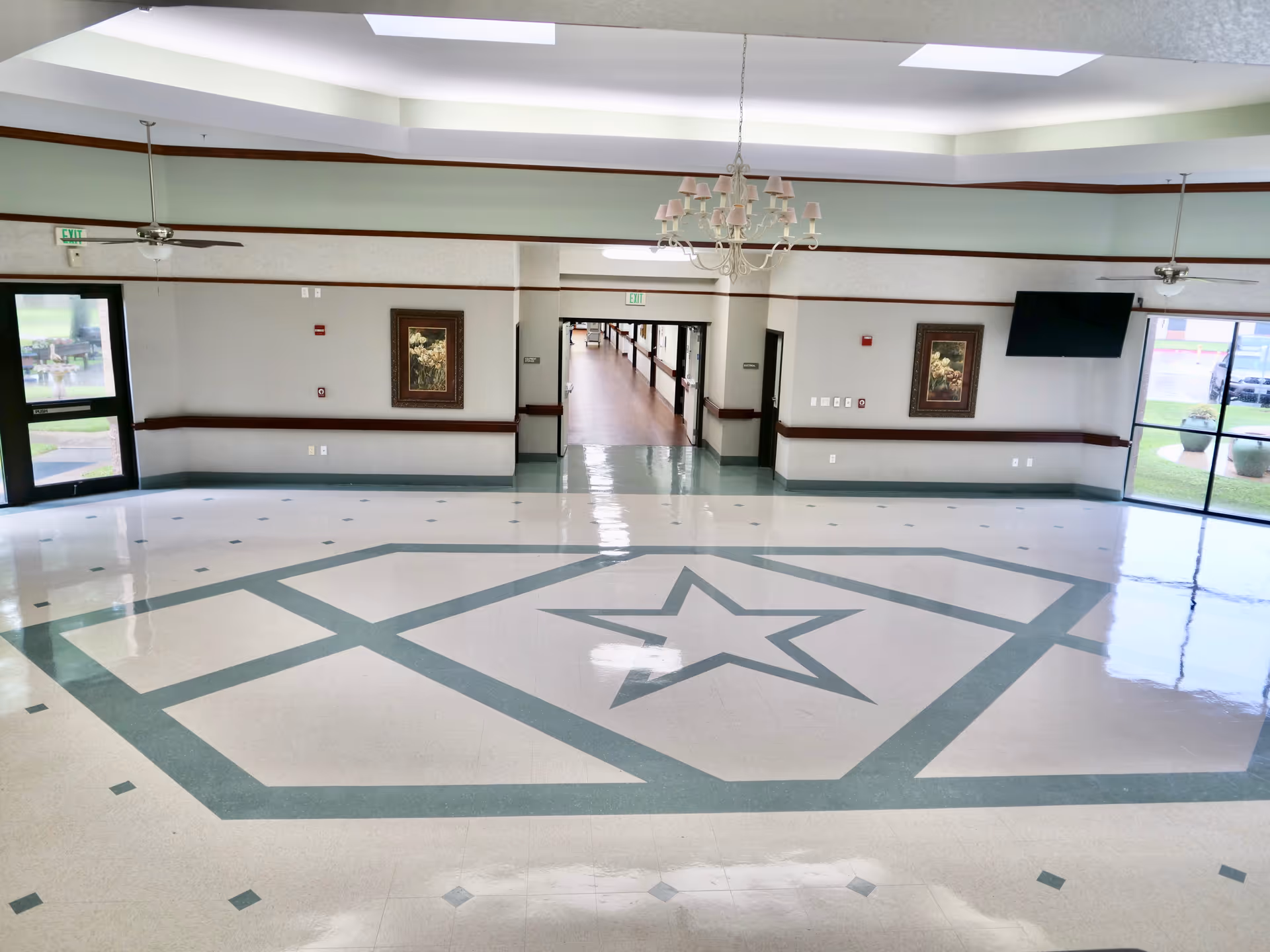 Spacious polished interior lobby with a large decorative star pattern on the floor, chandelier, hallway, and windows.