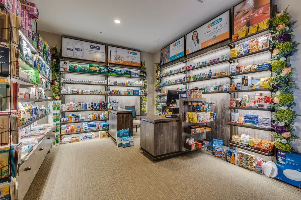 Small on-site convenience shop inside a senior living facility with shelves stocked with toiletries, snacks and a central checkout counter.