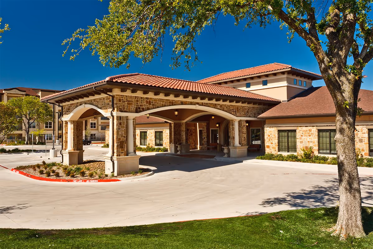 Stone-clad entrance and covered porte-cochère of The Villages of Lake Highlands with a tiled roof and circular driveway.