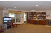 Spacious senior living common room with a TV and seating on the left, bookshelves and a fireplace on the right, and a door and windows at the back.