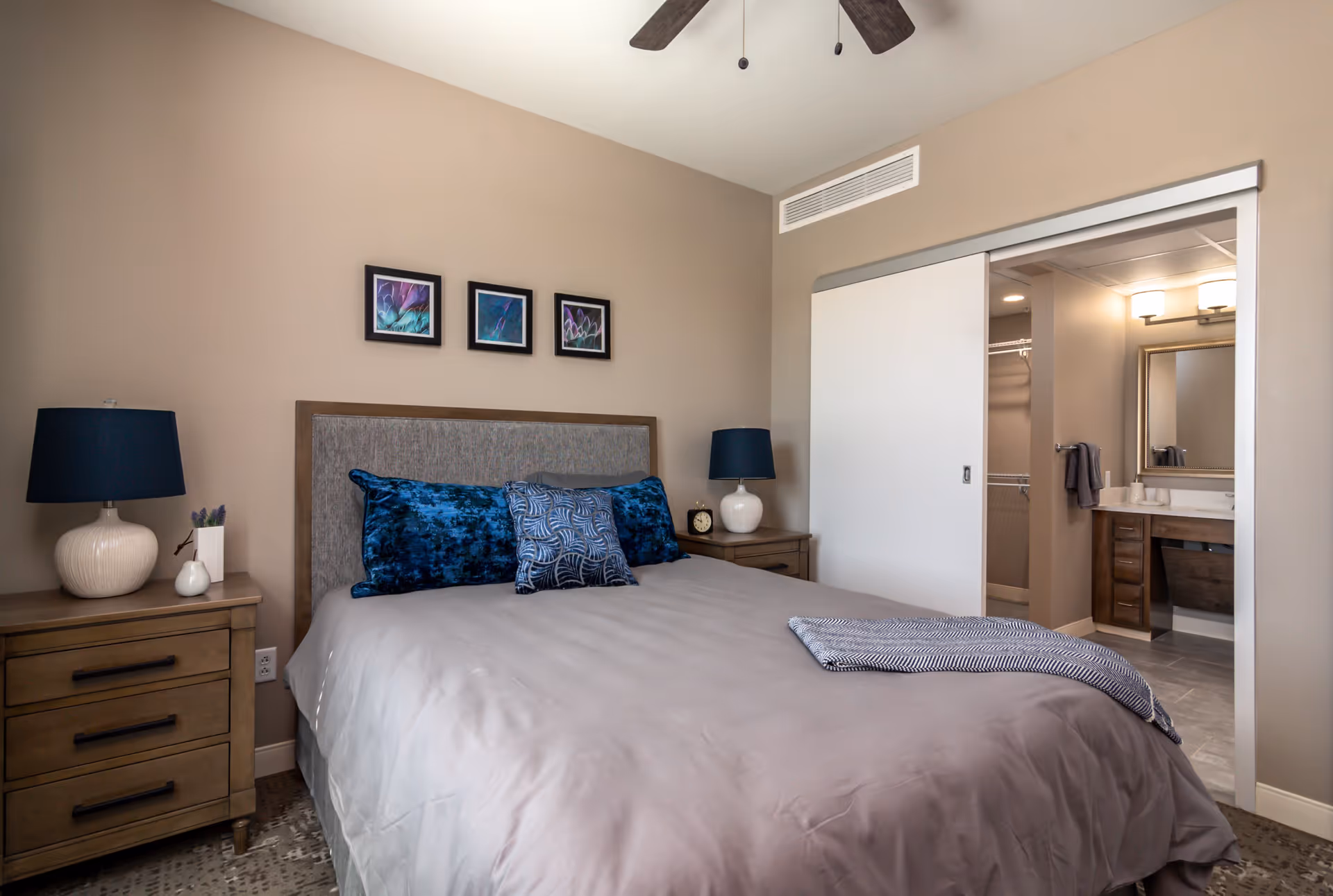 Well-appointed bedroom with a bed, nightstands and lamps, decorative pillows, and a sliding door opening to an en-suite bathroom.