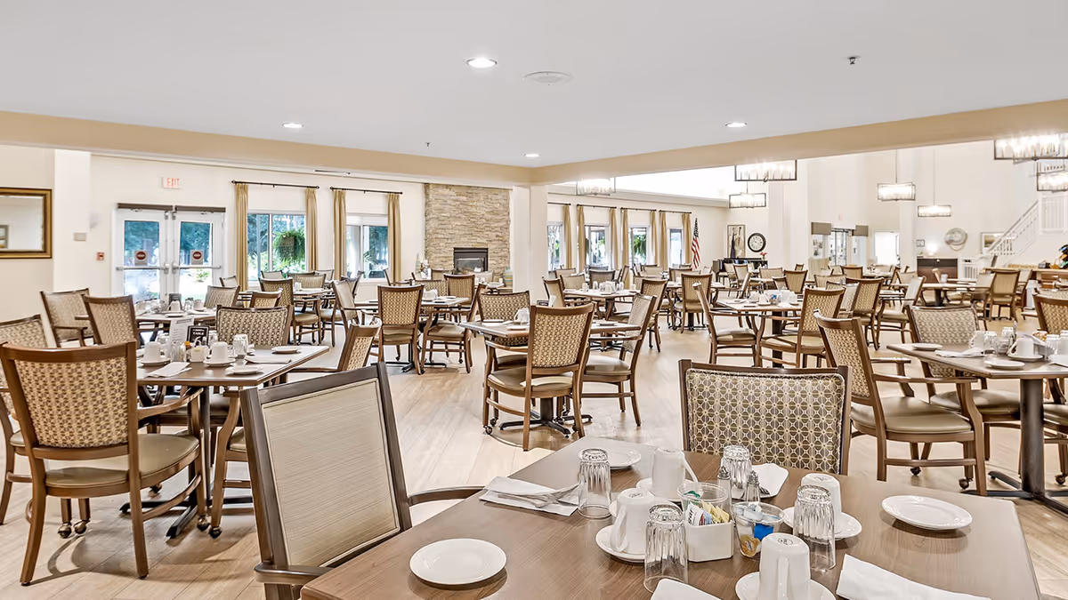 Interior view of the dining room at Holiday Indigo Pines, featuring tables set for dining, chairs, and large windows with natural light.