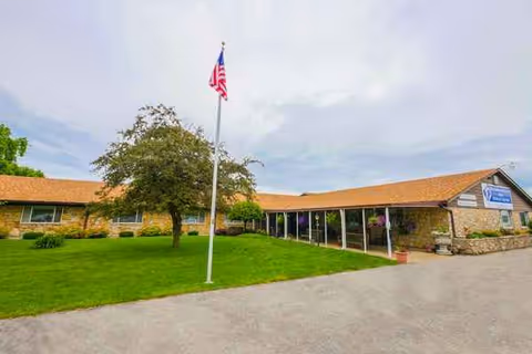 Single-story Waldron Rehabilitation and Healthcare Center exterior with flagpole and green lawn.