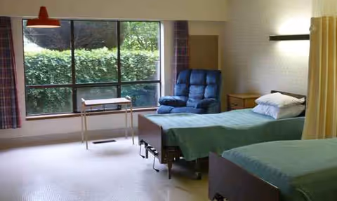Two hospital-style beds in a bright senior living bedroom with a blue recliner