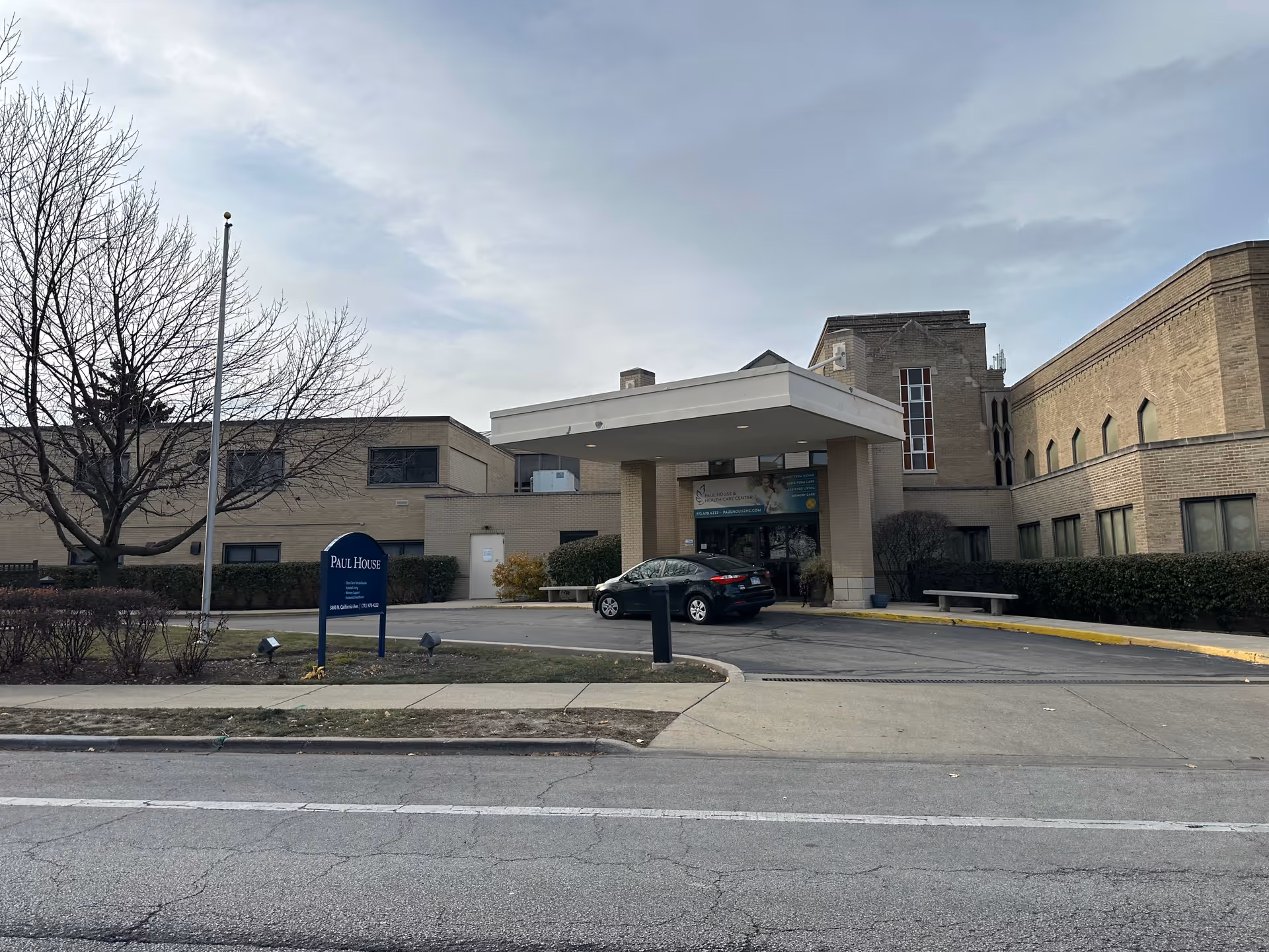 Front entrance of the Paul House and Healthcare Center building with a covered drive-up, a lawn sign, and a parked car.