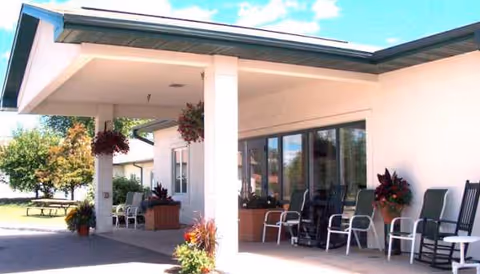 Exterior view of Newcare Residence entrance with covered porch, seating, and potted plants.