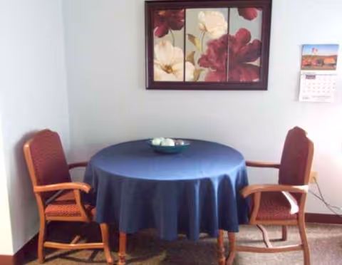 Small round table with a blue tablecloth, flanked by two red upholstered chairs in a corner.