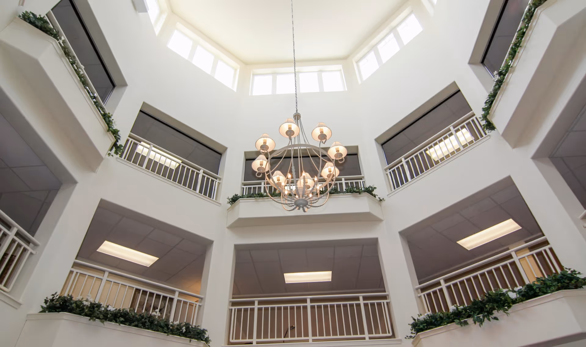 Multi-story interior atrium with a central chandelier, surrounding balconies and upper skylight windows.