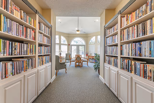 Hallway lined with built-in bookshelves opening to a bright seating area with tables and arched windows.