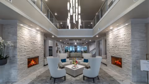 Spacious two-story modern lobby with seating area, stone-clad walls, twin fireplaces and a central chandelier.