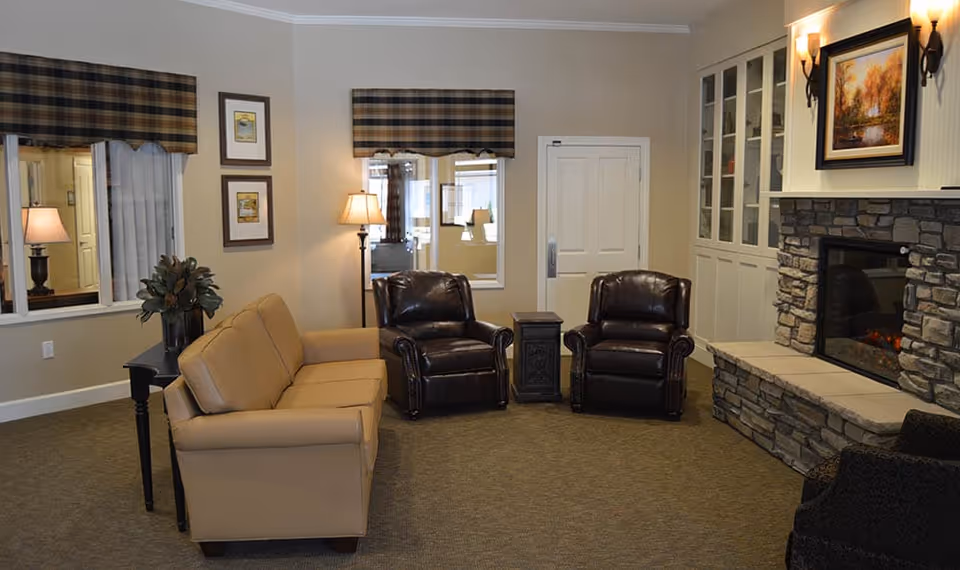 Cozy common living room with a sofa, two leather armchairs, side tables, and a stone fireplace.