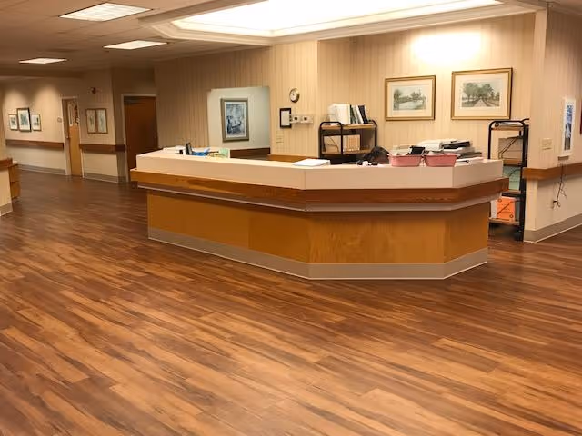Empty reception/nurses' station in a well-lit hallway with wood floors and framed pictures on the walls.