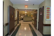 Corridor in a senior living facility with a shiny tiled floor, open double doors, and a nurses' station at the end.