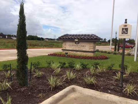 Entrance sign reads Clayton Oaks Living, surrounded by manicured landscaping and a handicap parking sign.