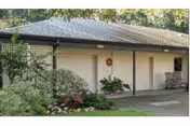 Single-story building exterior with a covered walkway, three white roll-up doors, columns, and landscaping in front.