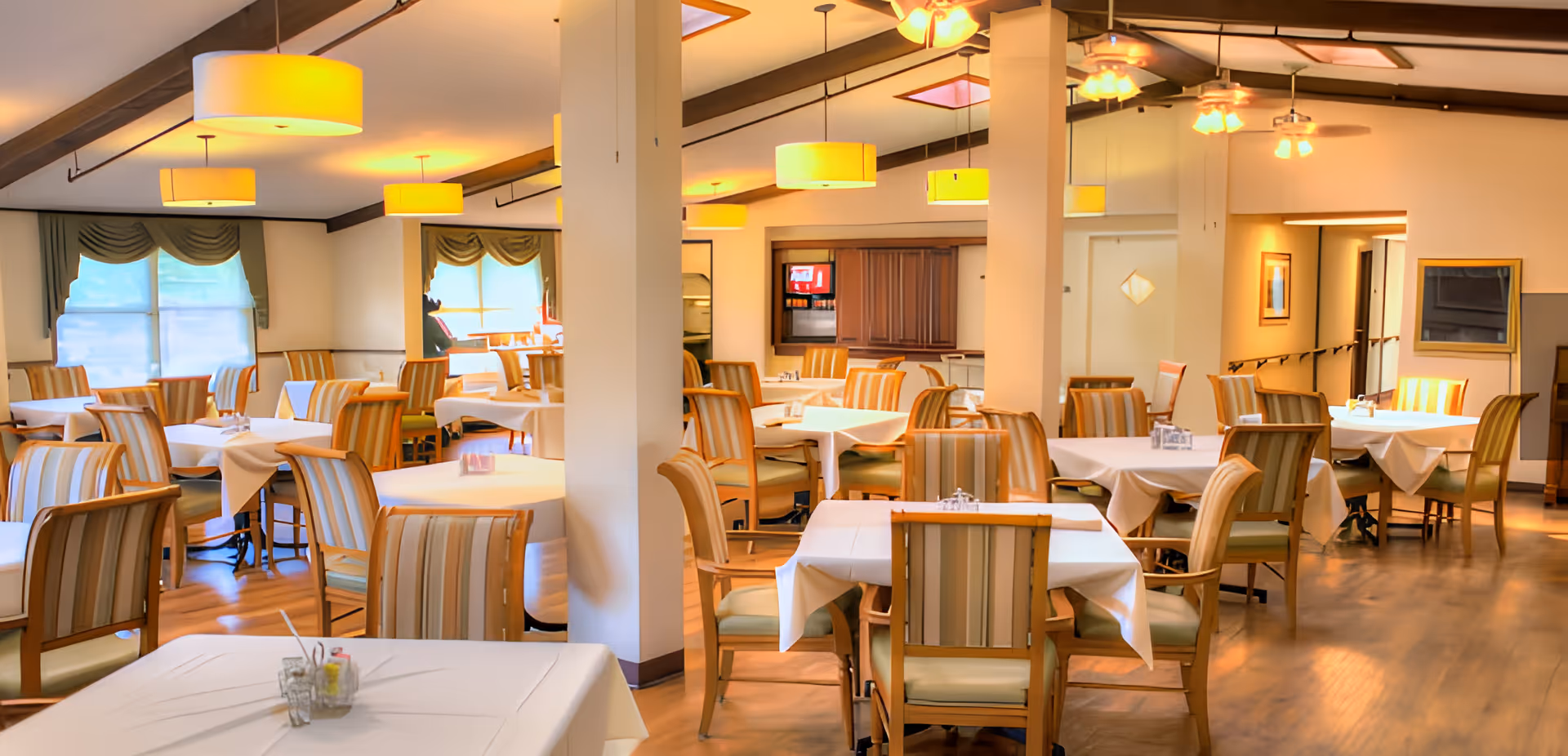 Spacious dining room with multiple tables covered in white linens and striped chairs under warm pendant lighting.