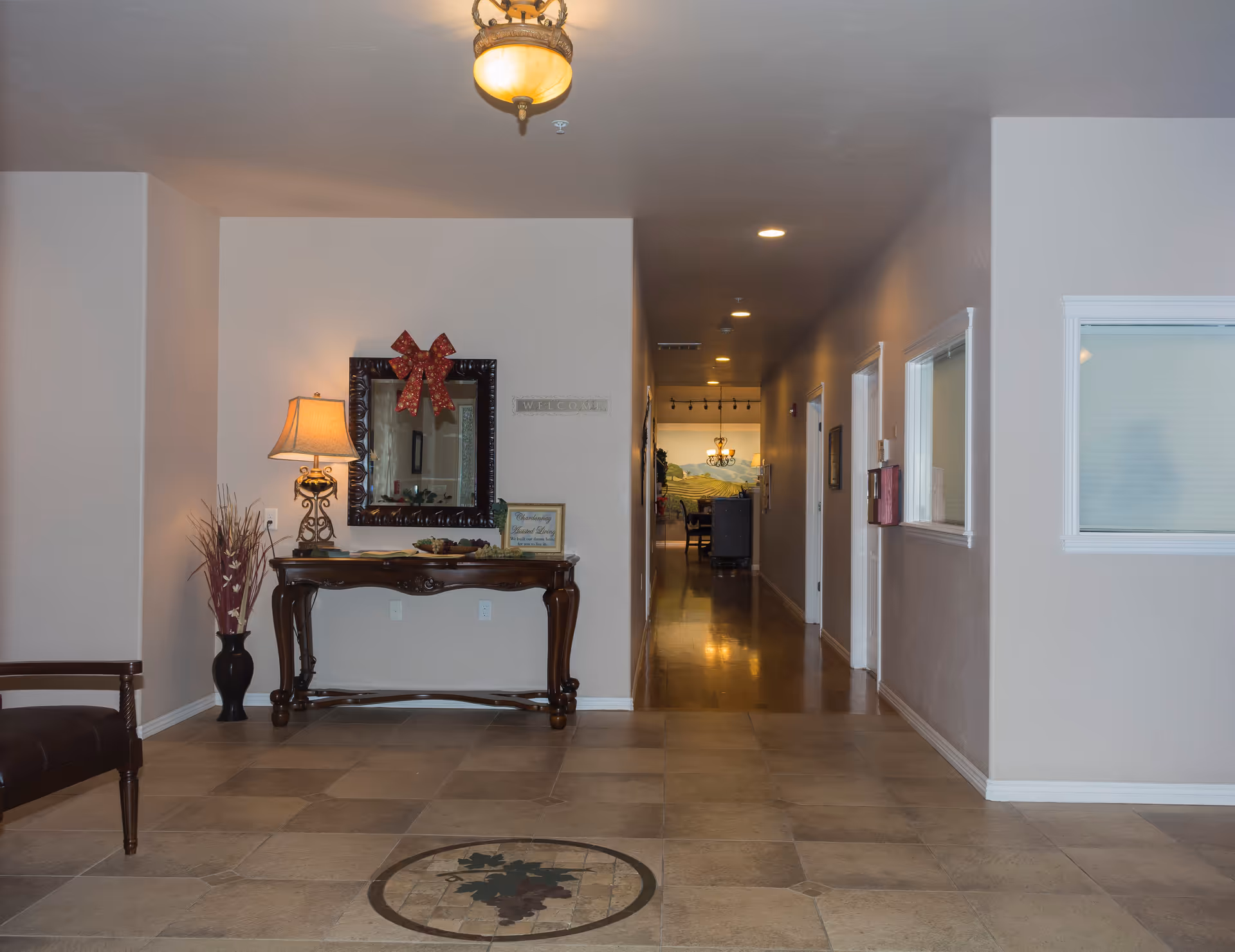 Interior entrance lobby with a decorative console table, mirror and lamp and a long hallway leading to common areas.