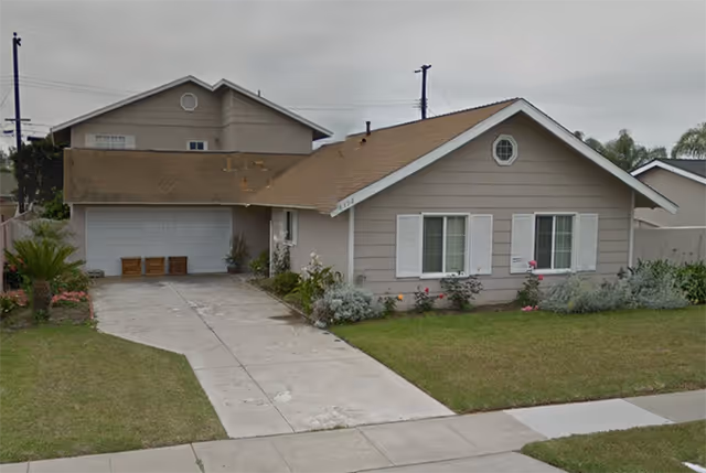 Front exterior view of a single-story residential house with a driveway, garage, and a well-maintained lawn with some shrubs and flowers.