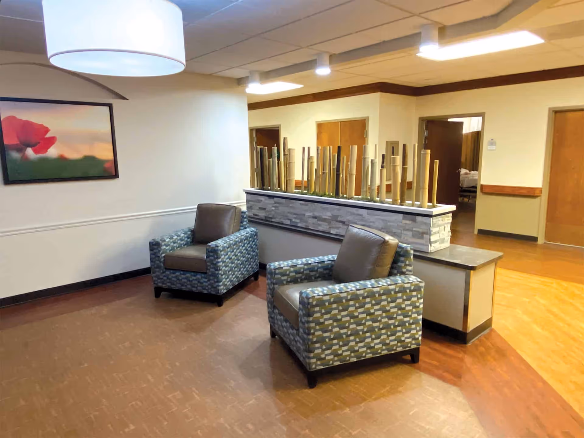 Two upholstered armchairs sit in a well-lit common seating area with a decorative divider and wall art.