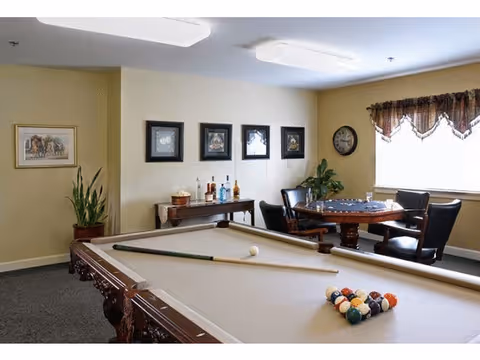 Game room featuring a pool table with cues and racked balls in the foreground and a card table with chairs near a window.