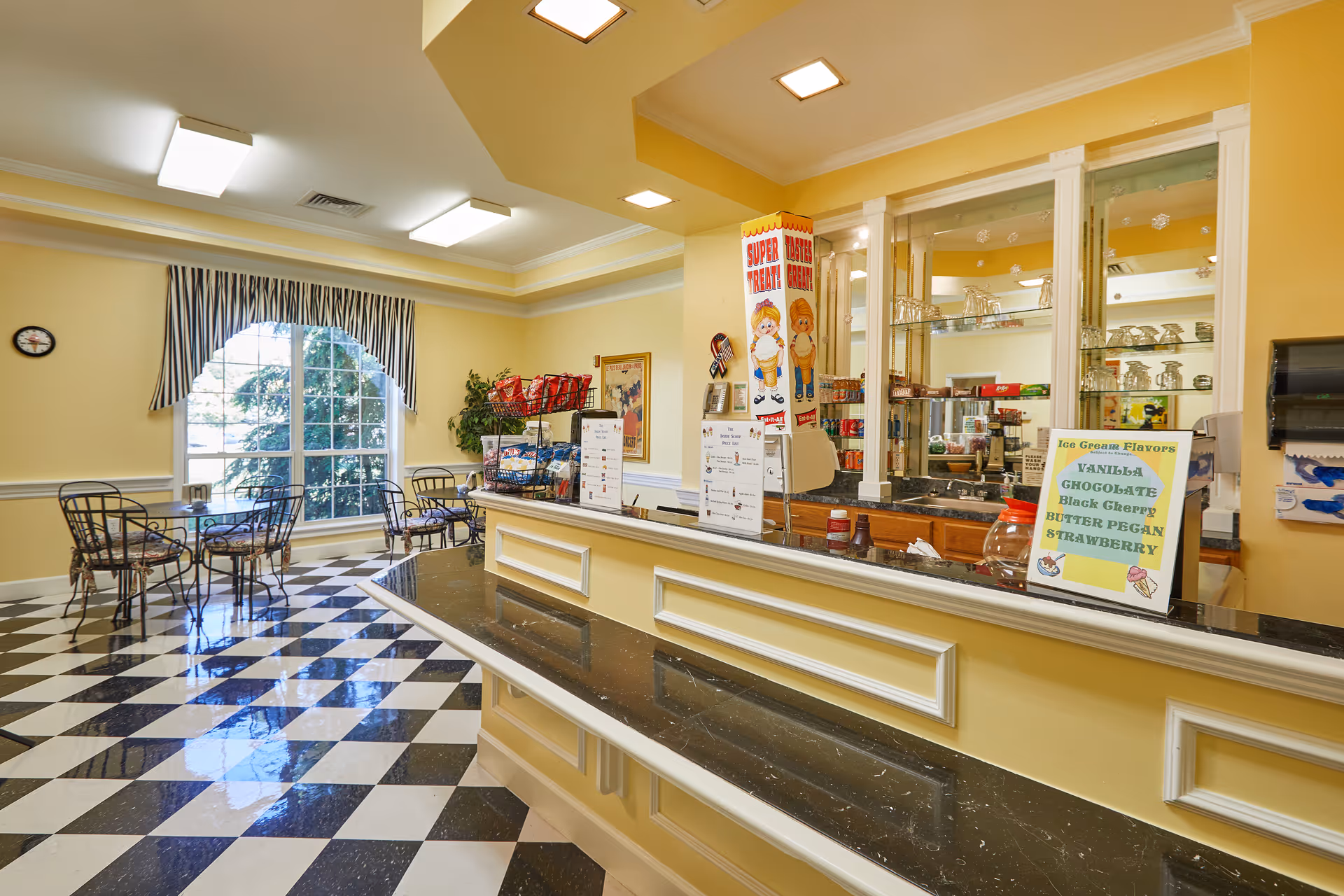 Bright snack bar area with a service counter, checkered floor and small café tables by a large arched window.