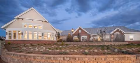 Exterior view of Brookdale Highlands Ranch front building with landscaping and stone wall at dusk.