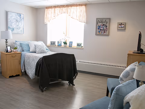 Bright furnished bedroom with a single bed, nightstand, seating, and wall decor.