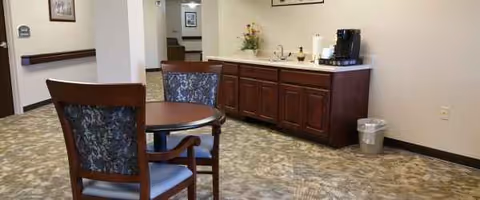 There is a small round table with two chairs beside a coffee station in a lounge.