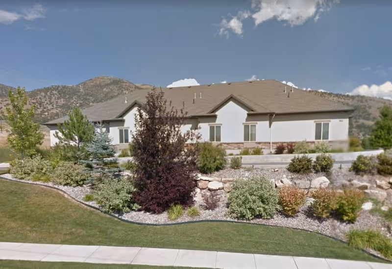 Single-story assisted living building with a landscaped front yard and mountains in the background.