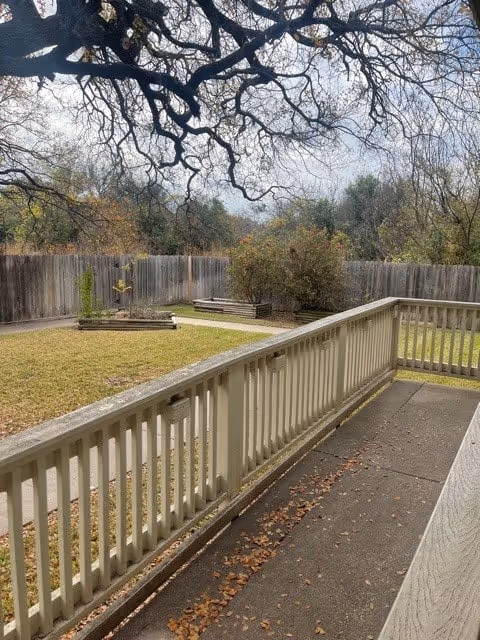 View from a porch railing over a fenced backyard with a grassy lawn, raised garden beds, and tree branches overhead.