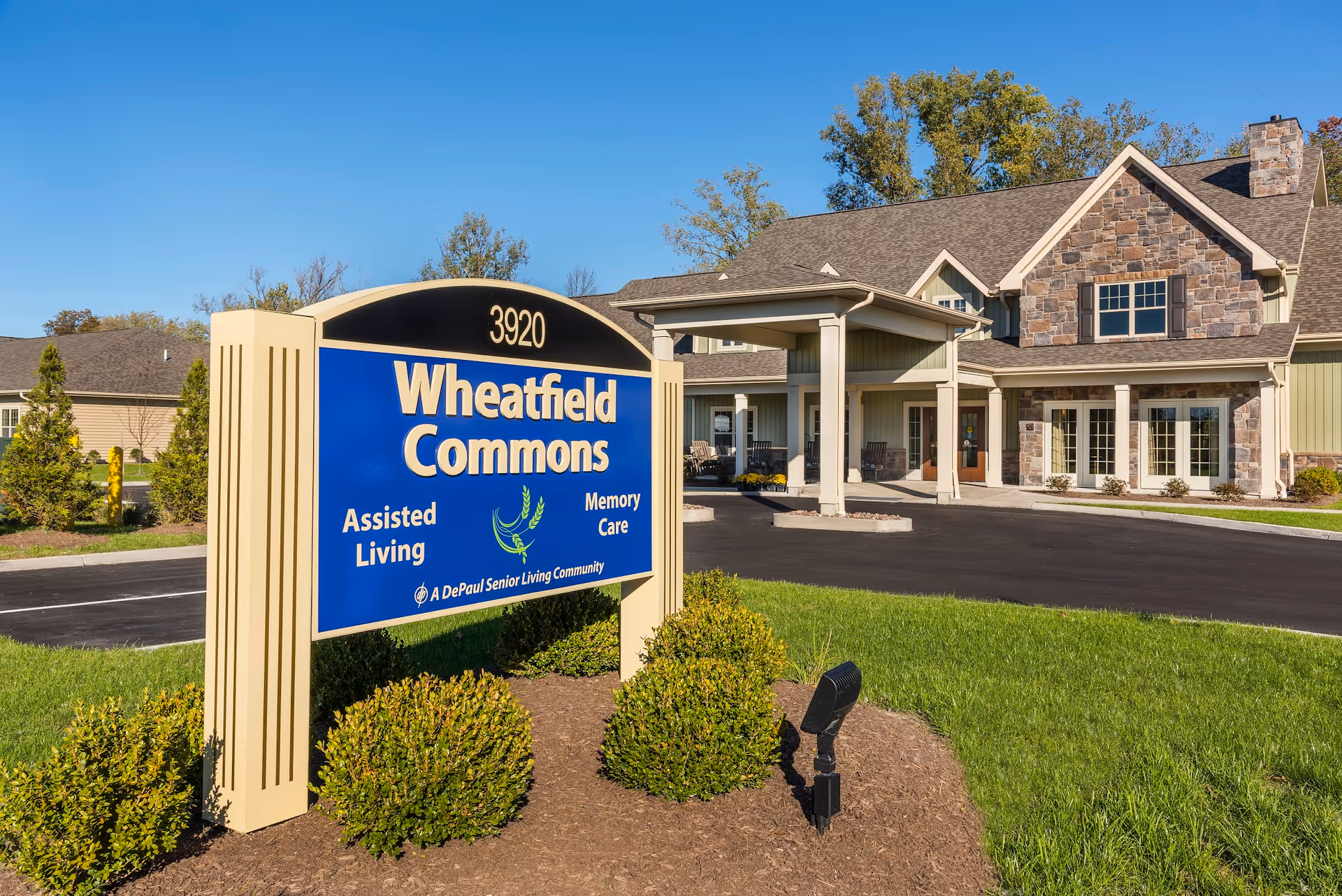Front exterior of Wheatfield Commons senior living building with a large blue sign and covered entrance.