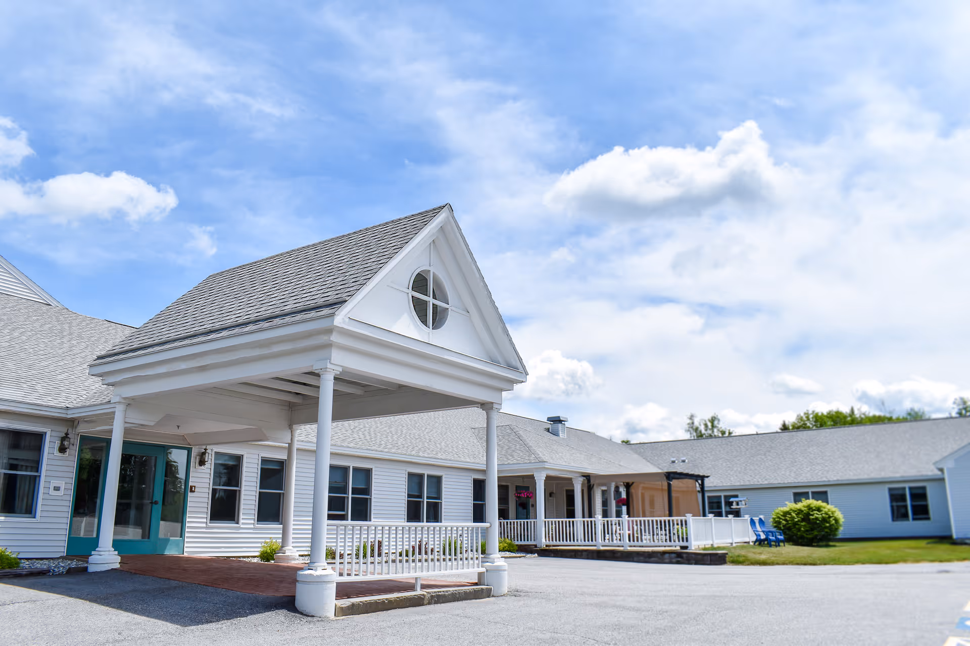 Covered front entrance and porch of a white single-story building under a blue sky.