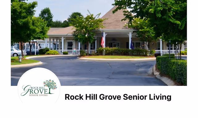 Front exterior view of Rock Hill Grove Senior Living facility with a circular driveway, trees, and an American flag near the entrance.