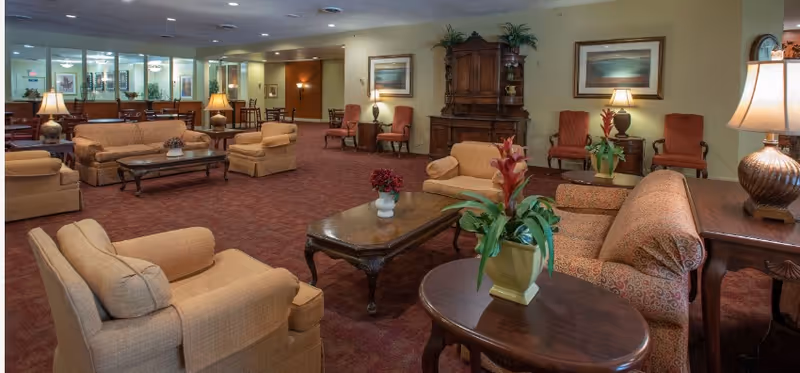 Spacious furnished common lounge with sofas, armchairs, coffee tables, lamps, and potted plants.