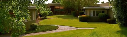 Well-manicured lawn surrounds low, mid-century retirement community buildings with a curved walkway.