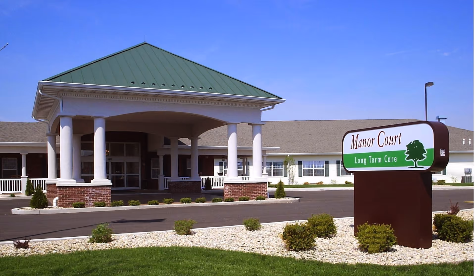 Exterior front entrance of a long-term care facility with a covered portico and a 'Manor Court Long Term Care' sign.