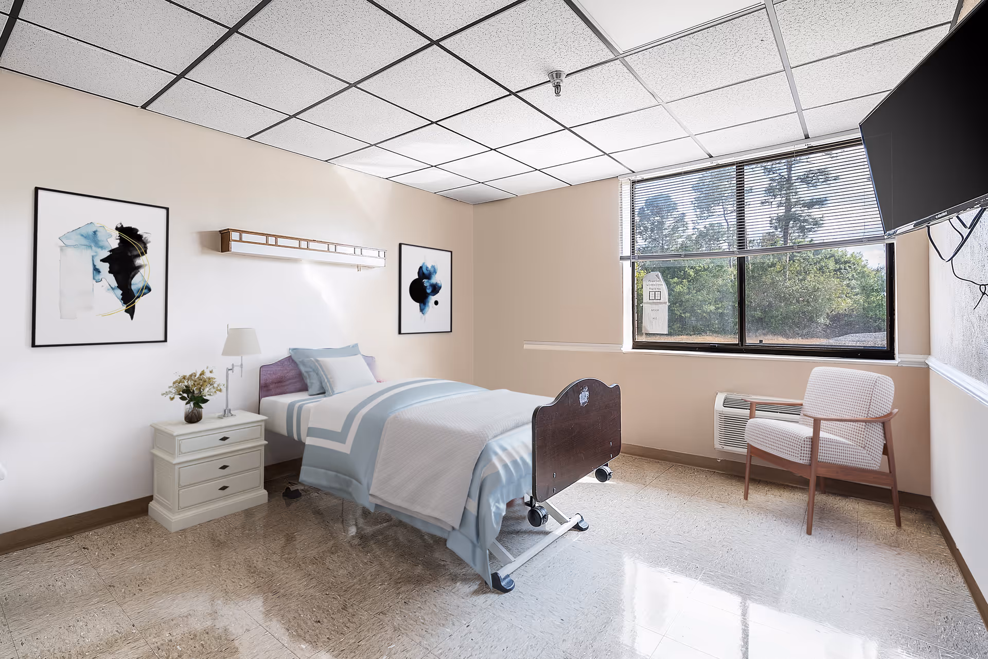 A bright and clean nursing center bedroom with a single hospital-style bed covered in light blue and white bedding. The room features a nightstand with a lamp and a small vase of flowers, two abstract paintings on the wall, a window with blinds showing greenery outside, a wall-mounted TV, and a cushioned armchair near the window.
