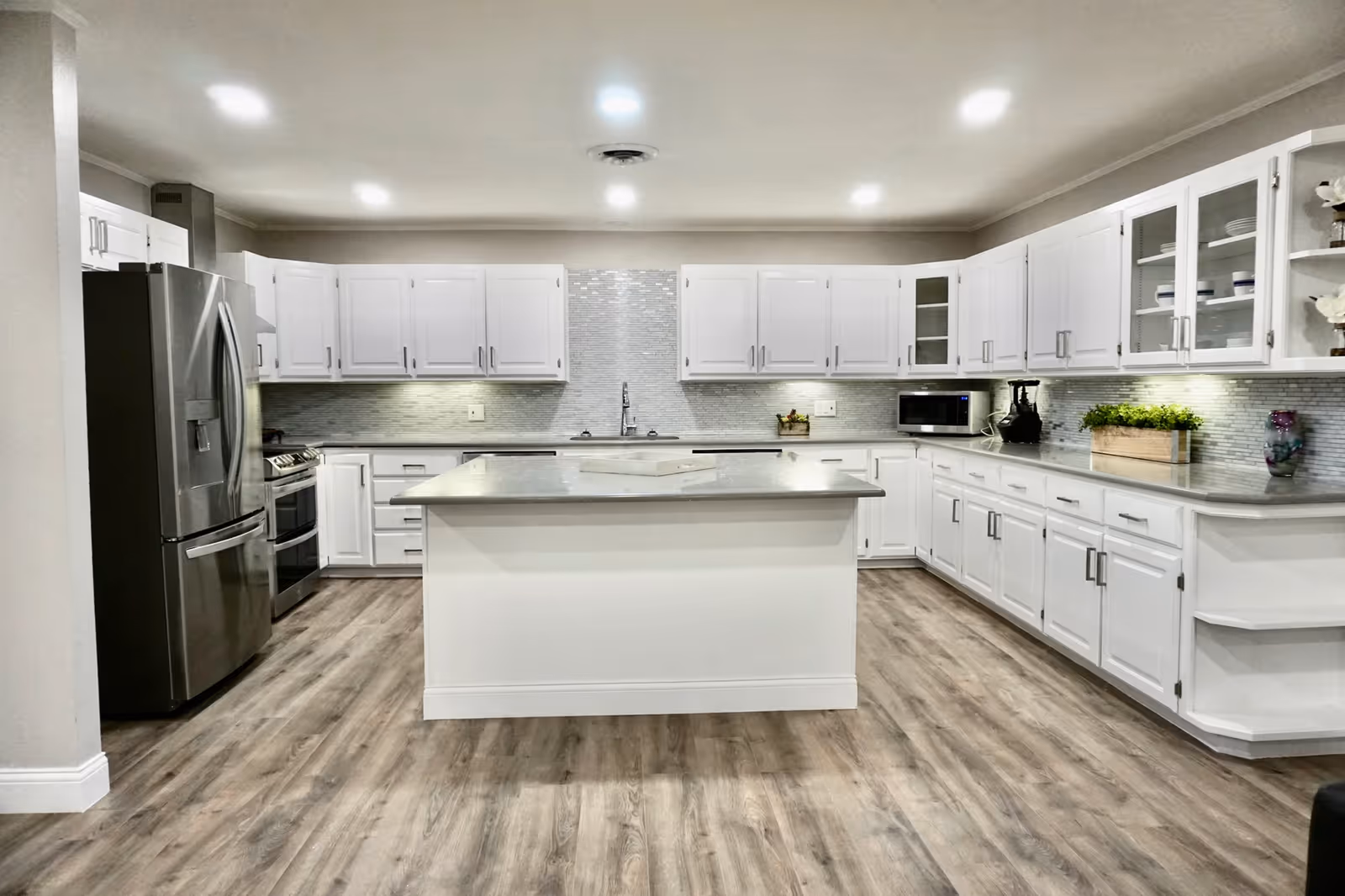 Bright modern kitchen with a large center island, white cabinets, stainless steel appliances, and wood-look flooring.
